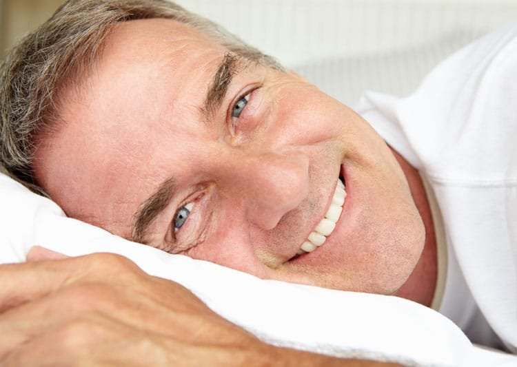 Man smiling while resting in bed, representing improved sleep after dental sleep apnea treatment.